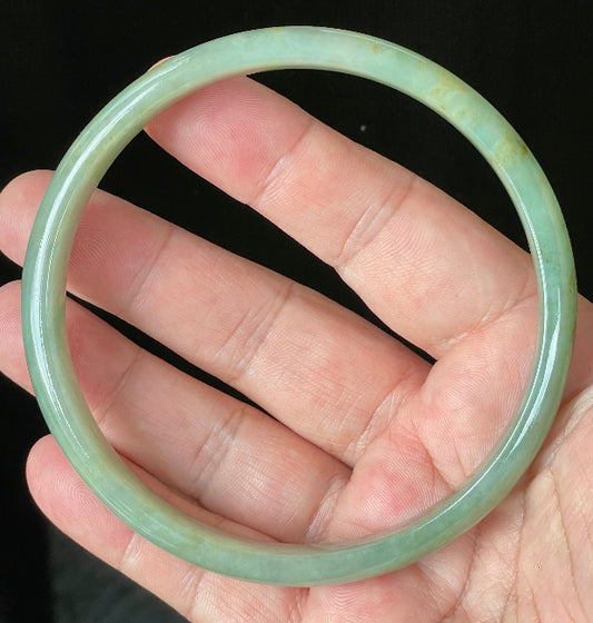 Hand holding a large 77.5mm certified Grade A Burmese jadeite bangle in icy imperial and apple green hues, item JB929