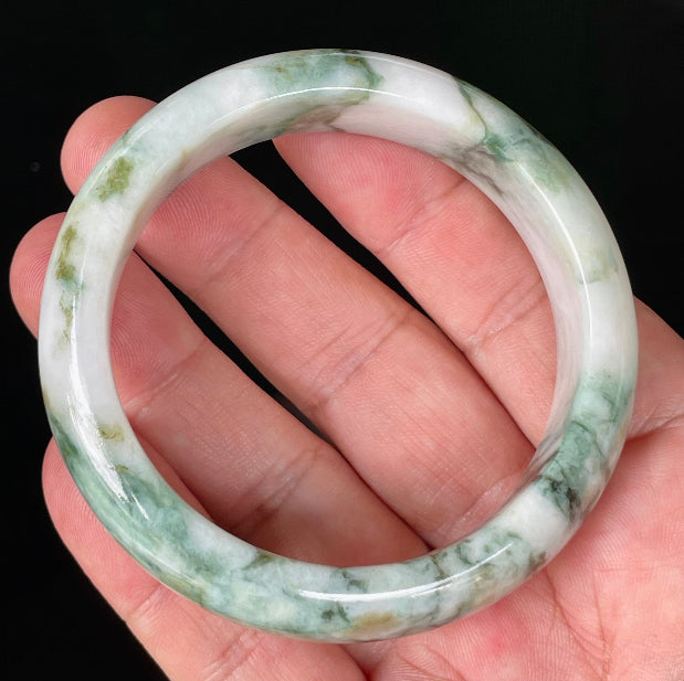 Hand holding a 57.8mm certified Grade A Burmese jadeite bangle in icy imperial green, apple green, and milky white hues, item JB877