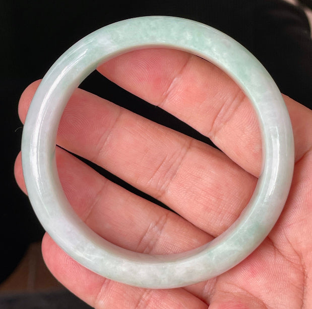 Hand holding a 58.3mm certified Grade A Burmese jadeite bangle in icy imperial green, apple green, and milky white hues, item JB875