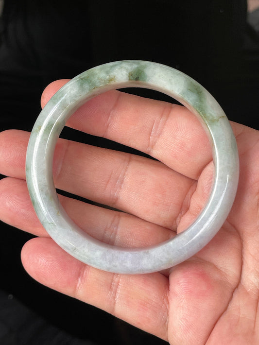 Hand holding a 56.7mm certified Grade A Burmese jadeite bangle in icy imperial and apple green with milky white and light lavender hues, item JB216