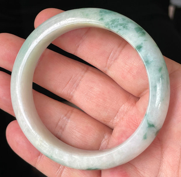 Hand holding a 58.5mm certified Grade A Burmese jadeite bangle in icy imperial green, milky white, and honeycomb hues, item JB214