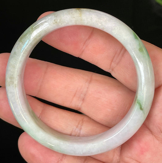 Hand holding a 54.5mm certified Grade A Burmese jadeite bangle in icy imperial and moss green with greyish milky white hues, item JB031