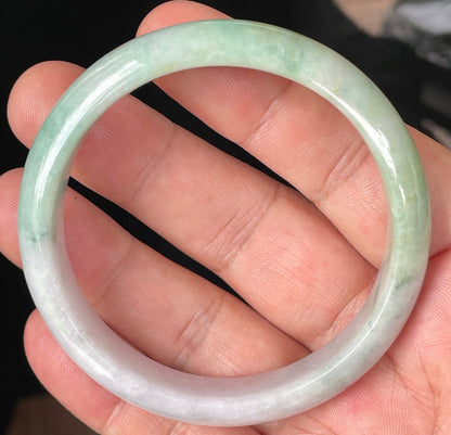 Hand holding a 57mm certified Grade A natural Burmese jadeite bangle in icy light lavender with imperial and apple green hues, item JB356