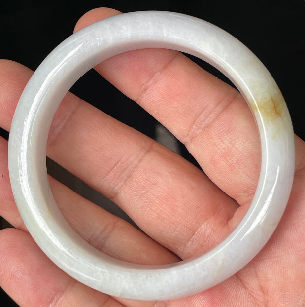 Hand holding a 57mm certified Grade A natural Burmese jadeite bangle in icy light lavender and milky white with honey hues, item JB359