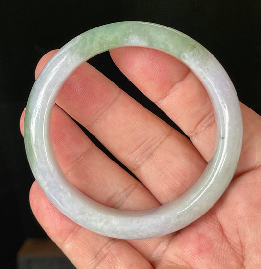 Hand holding a 55.2mm certified Grade A Burmese jadeite bangle in icy light lavender, milky white, and apple green hues, item JB854