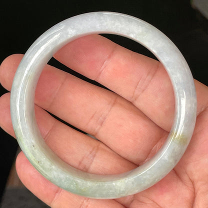 Hand holding a 58.3mm certified Grade A Burmese jadeite bangle in icy light lavender and milky white with apple green hues, item JB054