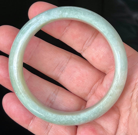 Hand holding a 58.2mm certified Grade A natural Burmese jadeite bangle in icy light apple green with milky white hues, item JB536