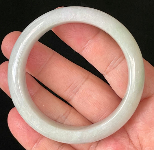 Hand holding a 55.5mm certified Grade A Burmese jadeite bangle in icy light apple green and milky white hues, item JB900