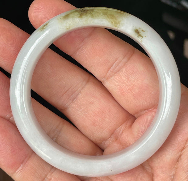 Hand holding a 53.4mm certified Grade A natural Burmese jadeite bangle in icy milky white with apple green and honey hues, item JB354