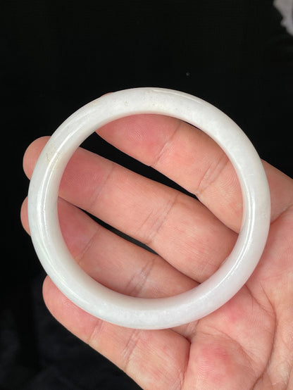 Hand holding a 58.5mm certified Grade A Burmese jadeite bangle in icy milky white and delicate honey hues, item JB827