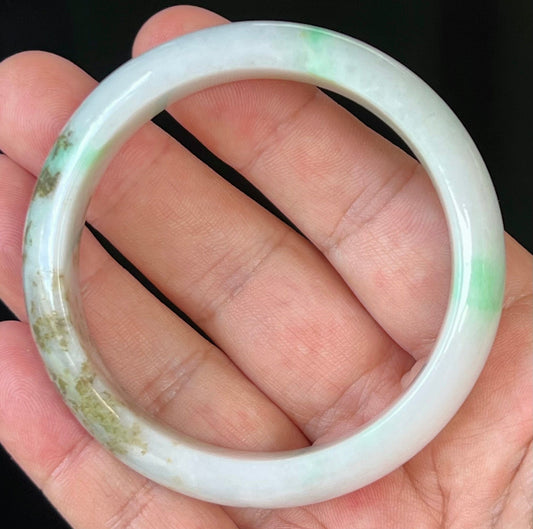 Hand holding a 56.7mm certified Grade A natural Burmese jadeite bangle in icy milky white with imperial and moss green, item JB527