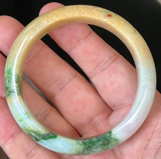 Hand holding a 58mm certified Grade A natural Burmese jadeite bangle in icy milky white with imperial green and honey yellow hues, item JB545