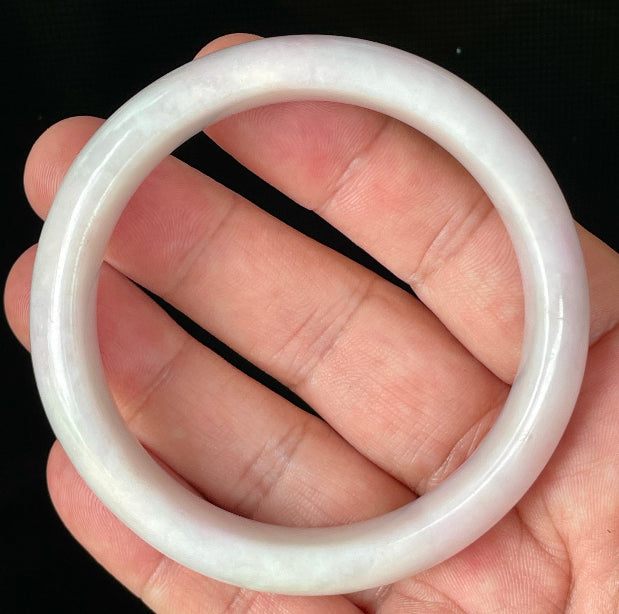 Hand holding a 58.5mm certified Grade A Burmese jadeite bangle in icy milky white with light lavender and apple green hues, item JB829
