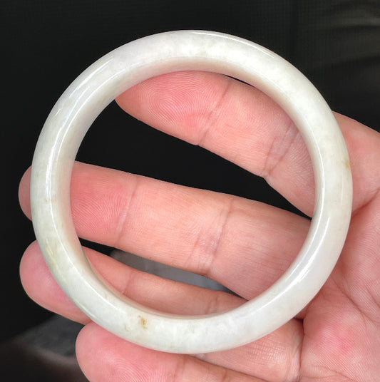 Hand holding a 57.4mm certified Grade A Burmese jadeite bangle in icy milky white with light yellow and honey hues, item JB805