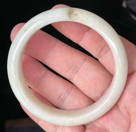 Hand holding a 59mm certified Grade A Burmese jadeite bangle in icy milky white with light yellow and honey hues, item JB928
