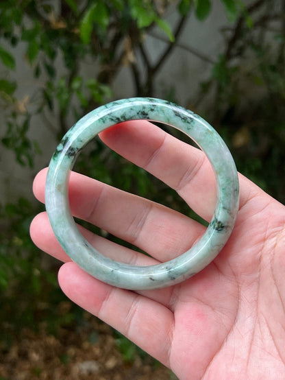 Hand holding a 62.1mm certified Grade A natural Burmese jadeite bangle in icy moss and snowflake green, item JB1302