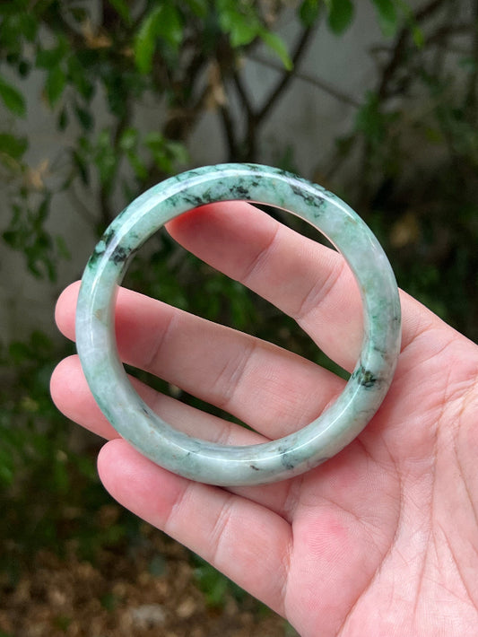 Hand holding a 62.1mm certified Grade A natural Burmese jadeite bangle in icy moss and snowflake green, item JB1302