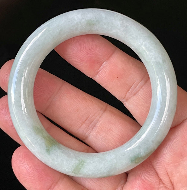 Hand holding a 52mm certified Grade A Burmese jadeite princess cut bangle in icy milky white and grey with imperial and apple green hues, item JB913