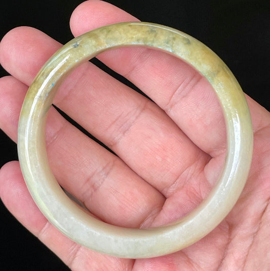 Hand holding a 58.3mm certified Grade A Burmese jadeite bangle in icy yellow and honey with apple and imperial green hues, item JB053