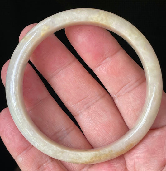 Hand holding a 59.5mm certified Grade A Burmese jadeite bangle in icy yellow, honey, milky white, and light lavender hues, item JB926