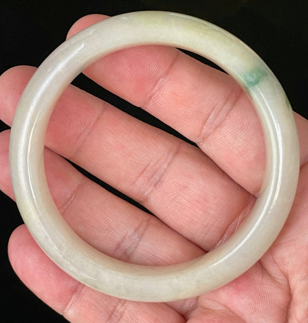 Hand holding a 56.1mm certified Grade A Burmese jadeite bangle in icy yellow and milky white with an imperial green hue, item JB109