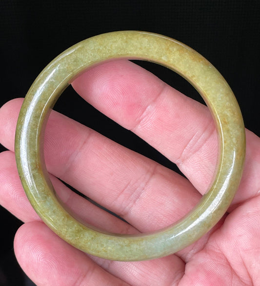 Hand holding a 52.4mm certified Grade A Burmese jadeite bangle in moss and apple green with brown hues, item JB872