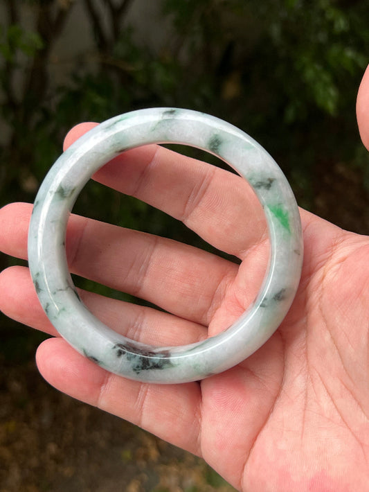 Hand holding a 62.7mm certified Grade A natural Burmese jadeite bangle in icy white and moss in snow green, item JB1315