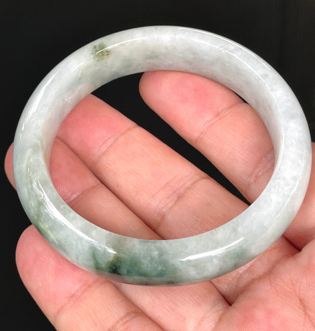 Hand holding a rare 54.7mm certified Grade A Burmese jadeite bangle in icy greyish milky white with imperial and apple green hues, item JB824