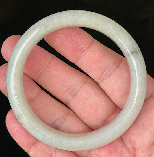 Hand holding a 58.7mm certified Grade A Burmese jadeite bangle in very icy apple green with an imperial green line, item JB200