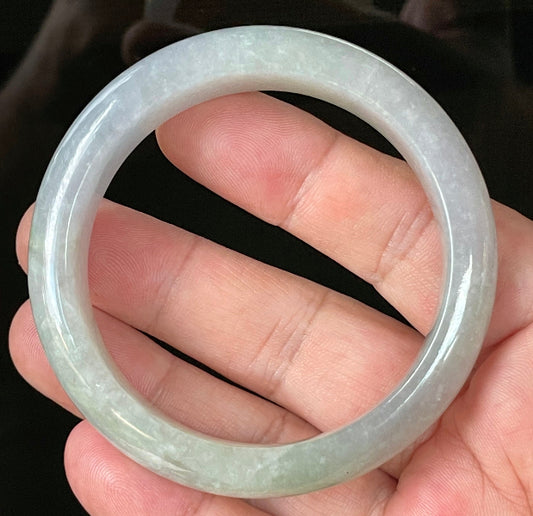 Hand holding a 55.9mm certified Grade A Burmese jadeite bangle in very icy light lavender and milky white with apple green hues, item JB126