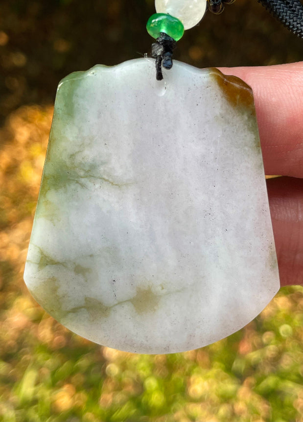 Untreated Type A Burmese jade pendant showing translucent luster with beautiful imperial green, white, and golden brown colors on an adjustable cord