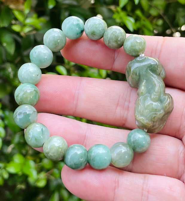 10mm certified Type A Burmese jade beads showing semi-translucent luster, mossy green hues, and a hand-carved Pixiu pendant on the wrist