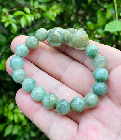10mm certified Type A Burmese jade beads showing semi-translucent luster, mossy green hues, and a hand-carved Pixiu pendant on the wrist