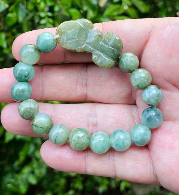 10mm certified Type A Burmese jade beads showing semi-translucent luster, mossy green hues, and a hand-carved Pixiu pendant on the wrist