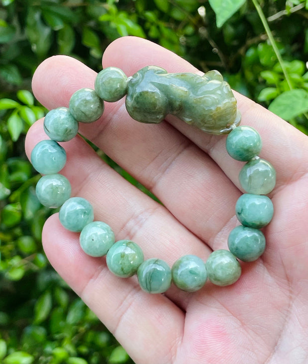 10mm certified Type A Burmese jade beads showing semi-translucent luster, mossy green hues, and a hand-carved Pixiu pendant on the wrist