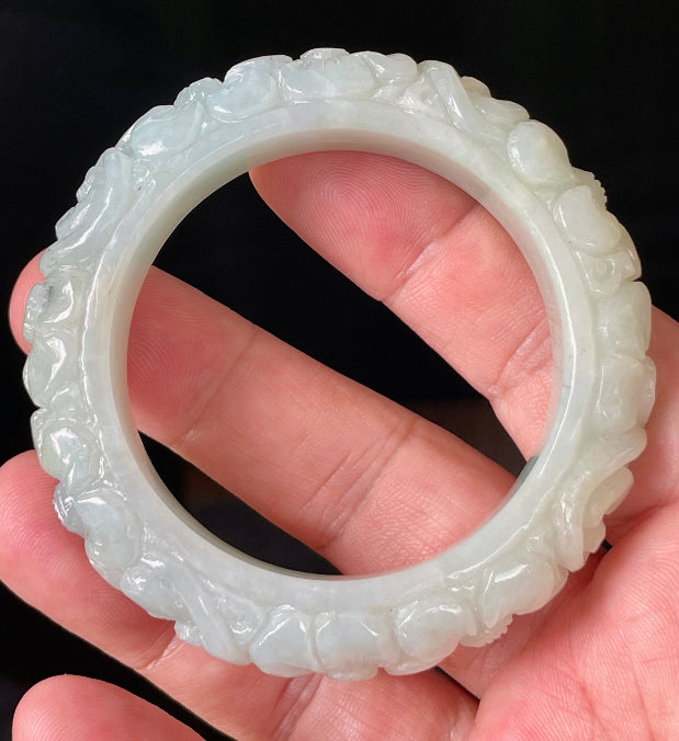 Close-up of a 50.7mm certified natural Grade A Burmese jadeite bangle featuring icy apple green hues and hand-carved floral motifs, item JB810