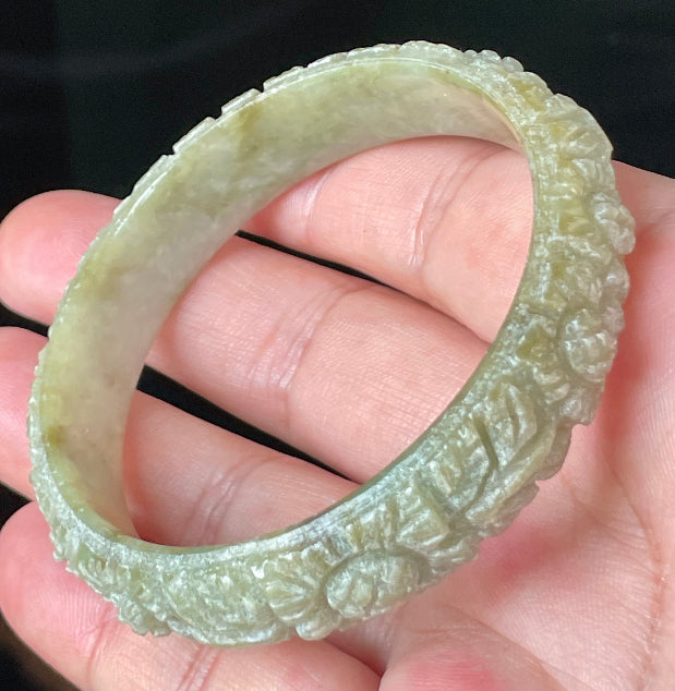 Close-up of a 57.4mm certified natural Grade A Burmese jadeite bangle featuring icy apple green and milky white hues with hand-carved floral motifs, item JB207