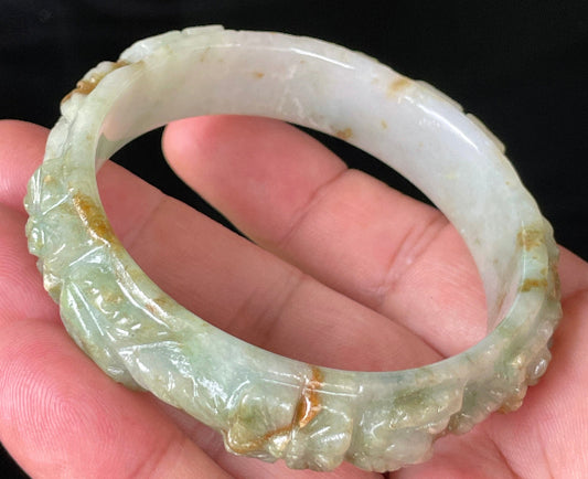 Close-up of a 57mm certified natural Grade A Burmese jadeite bangle featuring icy apple green, white, and honey hues with hand-carved floral motifs, item JB210