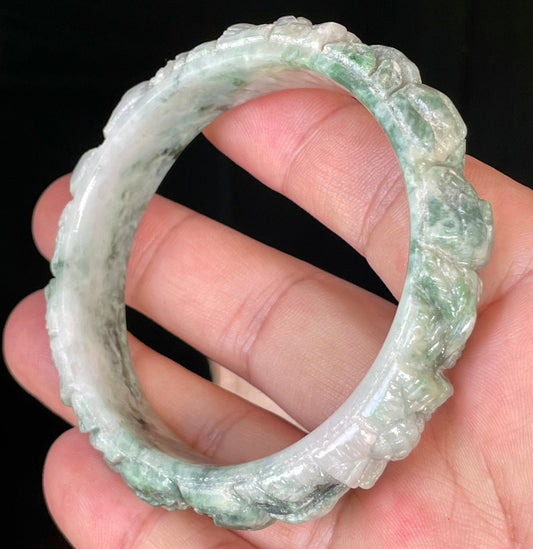 Close-up of a 56mm certified natural Grade A Burmese jadeite bangle featuring icy emerald green, imperial green, and milky white hues with hand-carved floral motifs, item JB443