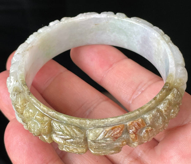 Close-up of a 58.7mm certified natural Grade A Burmese jadeite bangle featuring icy forest green, honey orange, and milky white hues with hand-carved floral motifs, item JB206
