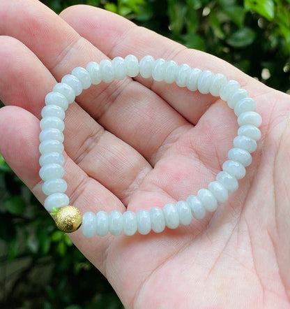 7.7mm natural Type A Burmese jade beads showing gentle translucency, icy green colors, and a matte gold accent on the wrist