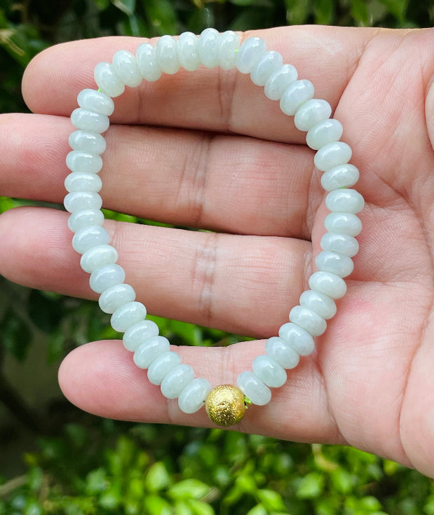 7.5mm natural Type A Burmese jade beads showing gentle translucency, icy green colors, and a matte gold-tone accent on the wrist