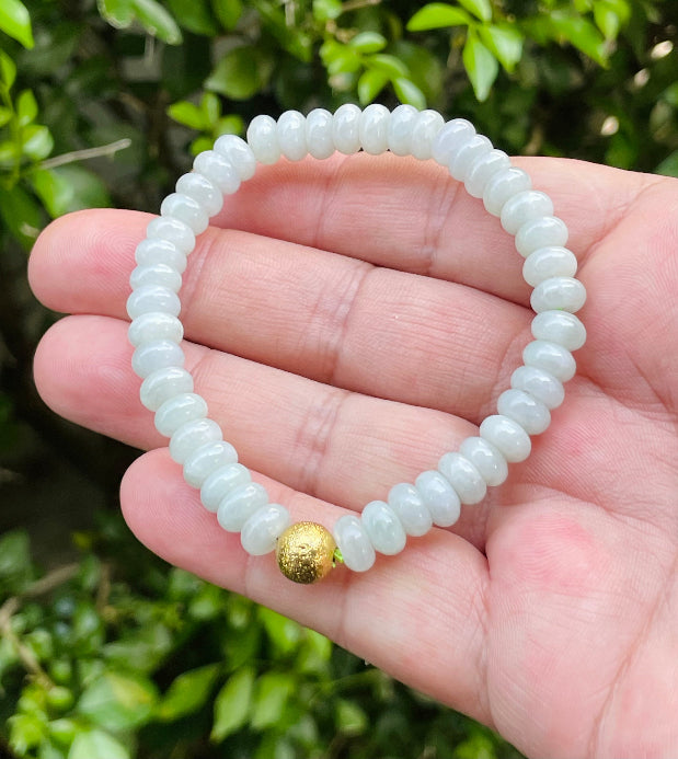 7.5mm natural Type A Burmese jade beads showing gentle translucency, icy green colors, and a matte gold-tone accent on the wrist