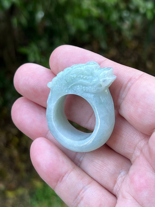 Hand holding a Size US 12.75 Grade A Burmese jadeite ring featuring a detailed hand-carved dragon motif in icy bluish white, item JDR003