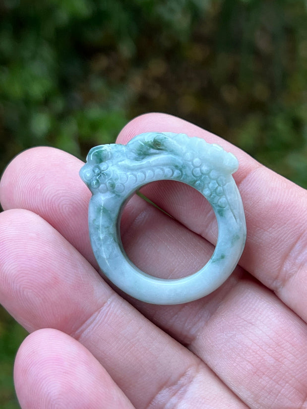 Hand holding a Size US 9.25 Grade A Burmese jadeite ring featuring a hand-carved dragon motif in icy white with moss green accents, item JDR002