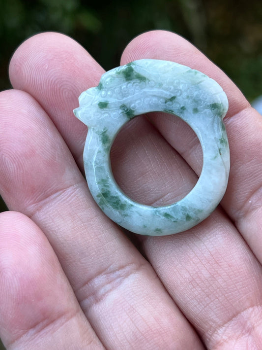Hand holding a Size US 9.5 Grade A Burmese jadeite ring featuring a hand-carved dragon motif in icy white with moss green inclusions, item JDR005