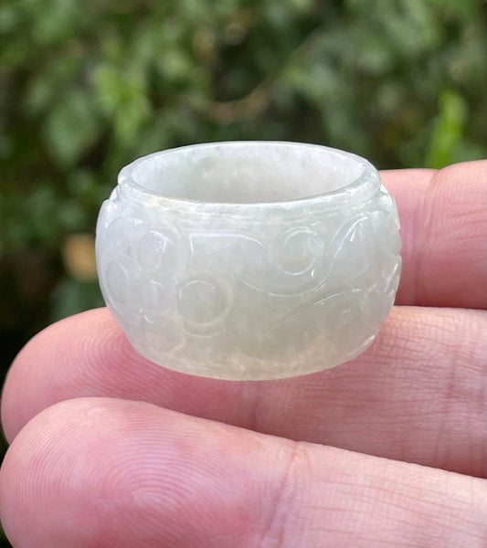Hand holding a Size US 11.5 Grade A Burmese jadeite thumb ring featuring a hand-carved swirling cloud motif in icy milky white and imperial green, item JRN035