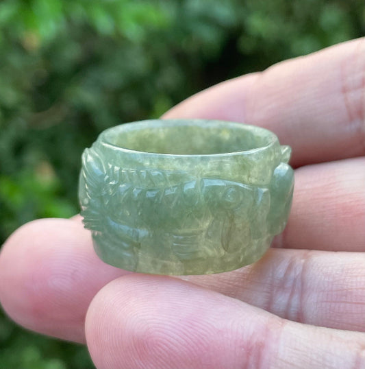 Hand holding a Size US 11.5 Grade A Burmese jadeite thumb ring featuring an intricately hand-carved fish motif in icy translucent emerald green, item JRN032
