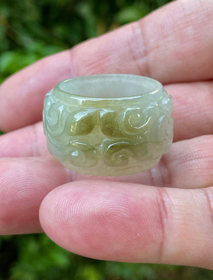 Hand holding a Size US 11.5 Grade A Burmese jadeite thumb ring featuring a hand-carved floral and swirl motif in icy apple green and spinach green, item JRN036