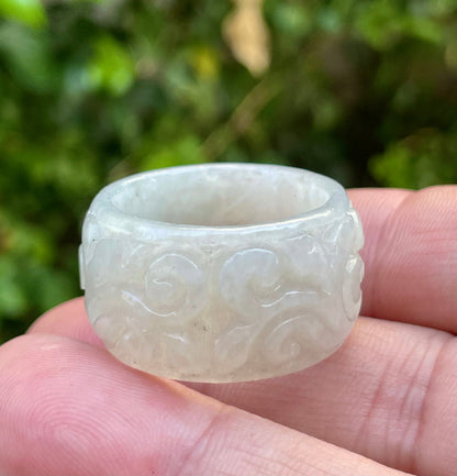 Hand holding a Size US 11.5 Grade A Burmese jadeite thumb ring featuring an intricately hand-carved floral and swirl motif in icy translucent light apple green, item JRN033